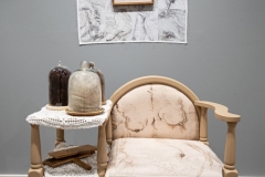Están Aquí Installation, 2024-26, repurposed object Gossip chair, specialty fabric, Botonaduras, artist’s grandmother’s wool cards, brown felt, antique white fringe trim, clear glass cloche domes, gray, red & brunette hair, fabric arches, hand-sewn human hair, patch on unprimed canvas, 34 3/4” x 36” x 17”, installed at Martin Museum of Art, Waco, Texas, 2026